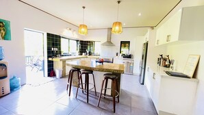 A modern kitchen with a central island, bar stools, pendant lighting, and a refrigerator. - Inave Oasis Villa ‘ Your home away from Home’ (Arorangi)