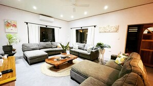 A modern living room with two grey sofas, a wooden coffee table, and a brown sofa. There are potted plants and artwork on the walls. - Inave Oasis Villa ‘ Your home away from Home’ (Arorangi)