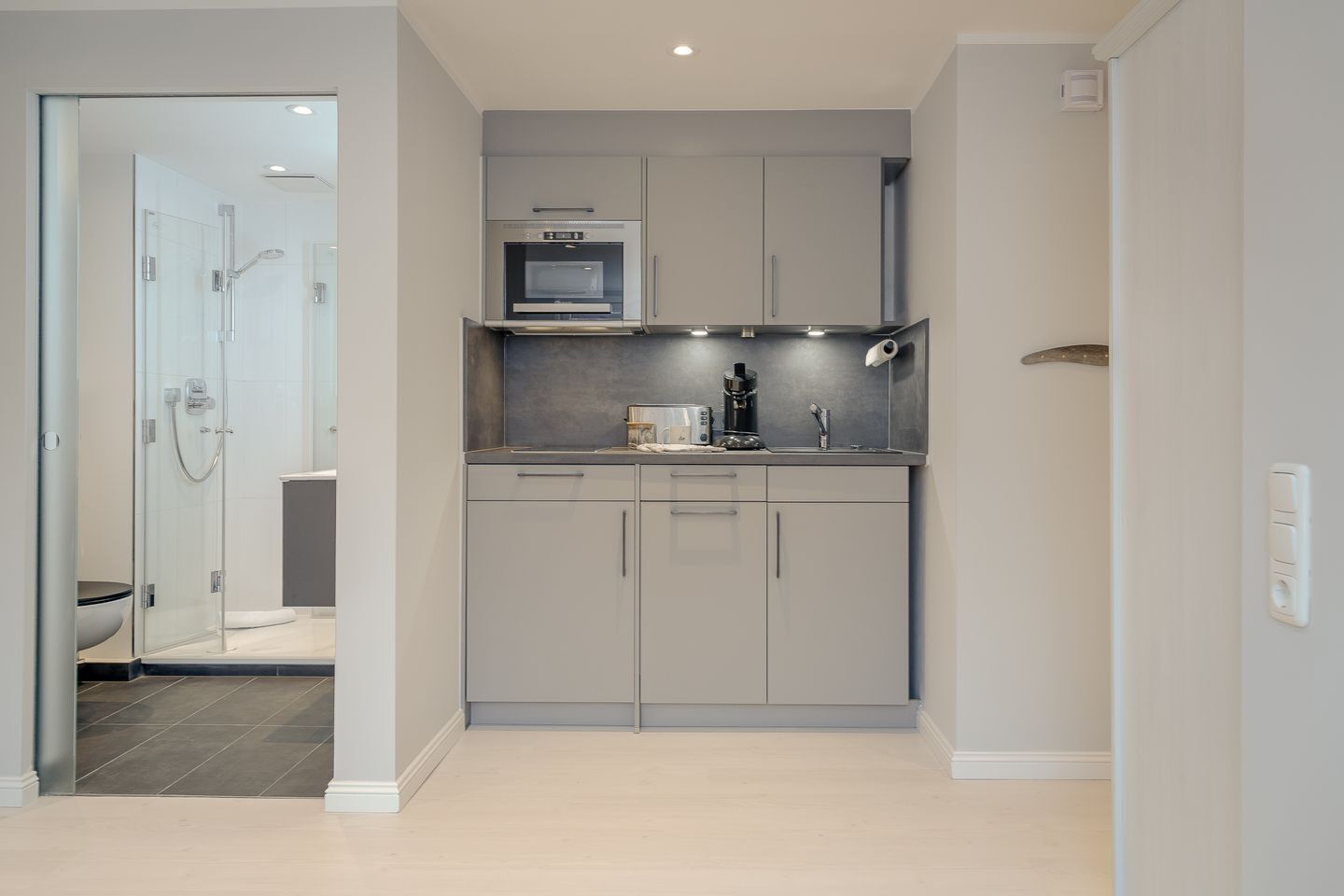A modern kitchen with grey cabinets, a built-in oven, and a coffee machine.