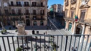 Un patio con una estatua, edificios con balcones y una calle con gente.