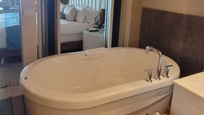 A modern bathroom with a freestanding bathtub, a wooden side table with toiletries, and a large mirror. - Stunning Loft Grand Luxxe (Nuevo Vallarta)