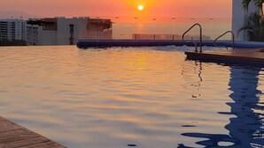 A swimming pool with a sunset view, a wooden deck, and a bridge overhead. - Stunning Loft Grand Luxxe (Nuevo Vallarta)