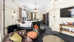 A hotel room with a bed, a seating area with a leather couch and armchair, a small table, and a television. - Hotel Queanbeyan Canberra (Queanbeyan)