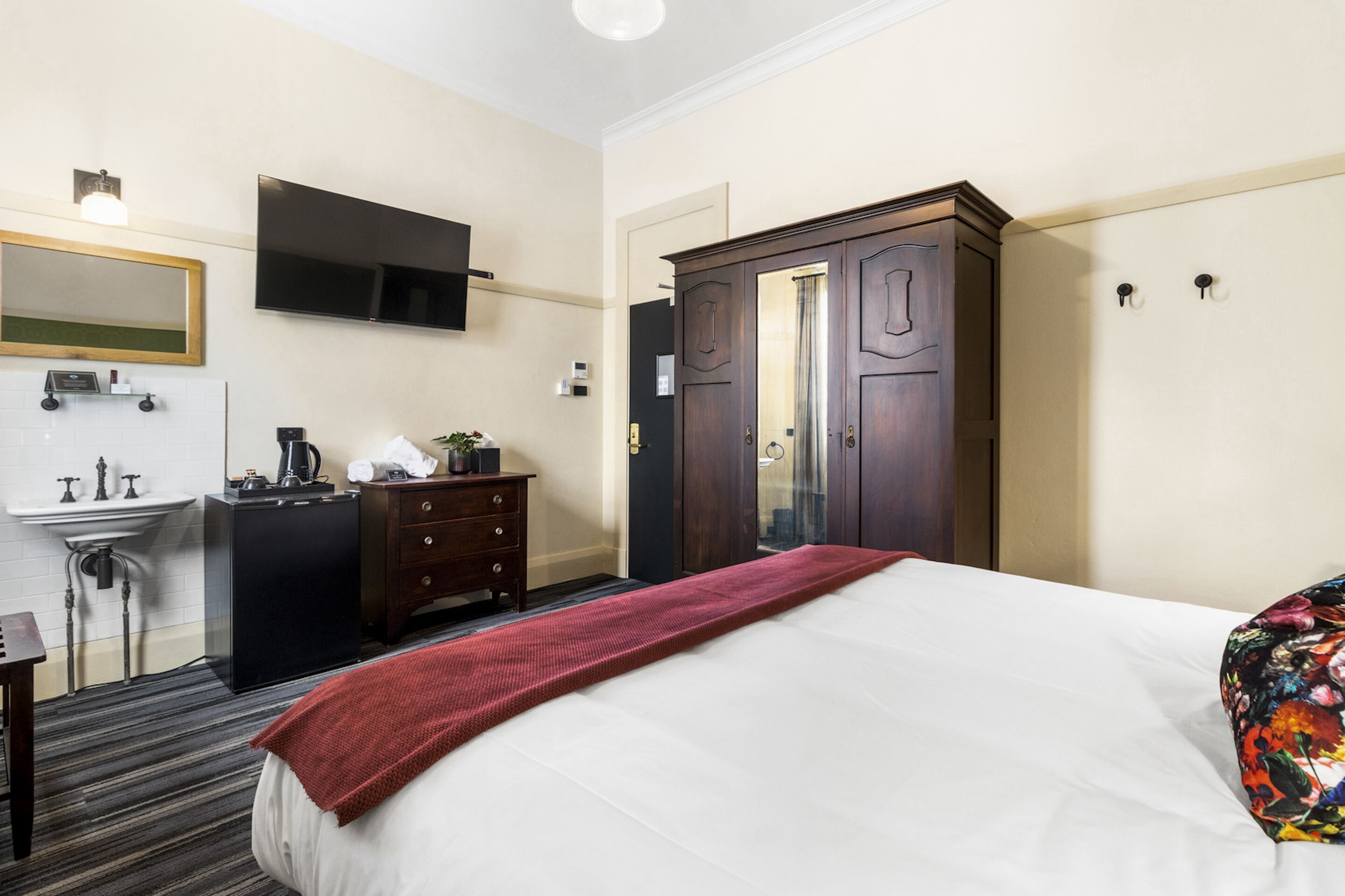 A hotel room with a bed, a dresser, a mirror, a TV mounted on the wall, and a wardrobe.