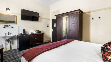 Habitación de hotel con cama, cómoda, espejo, televisor montado en la pared y armario.