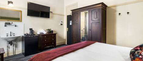 A hotel room with a bed, a dresser, a mirror, a TV mounted on the wall, and a wardrobe.