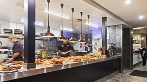 A modern kitchen with stainless steel counters, hanging pendant lights, and a herringbone-patterned floor. - Hotel Queanbeyan Canberra (Queanbeyan)