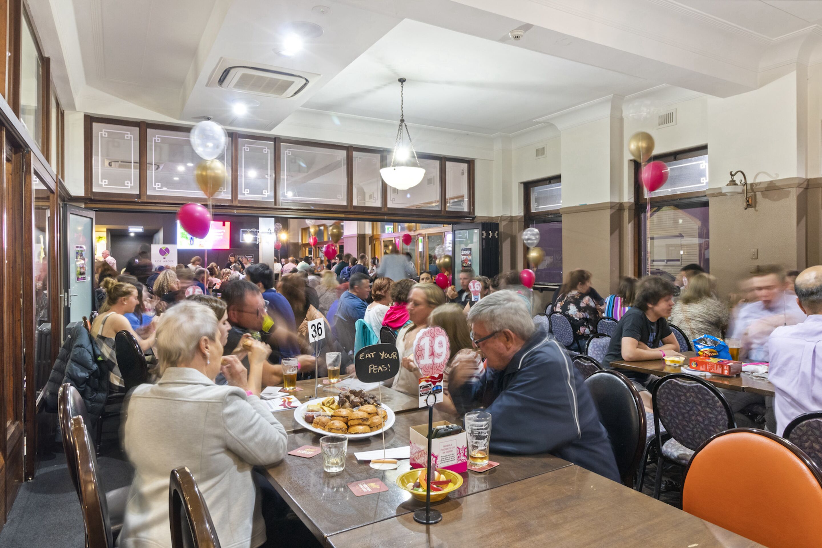 Un restaurante concurrido con mesas y sillas de madera, y personas cenando.