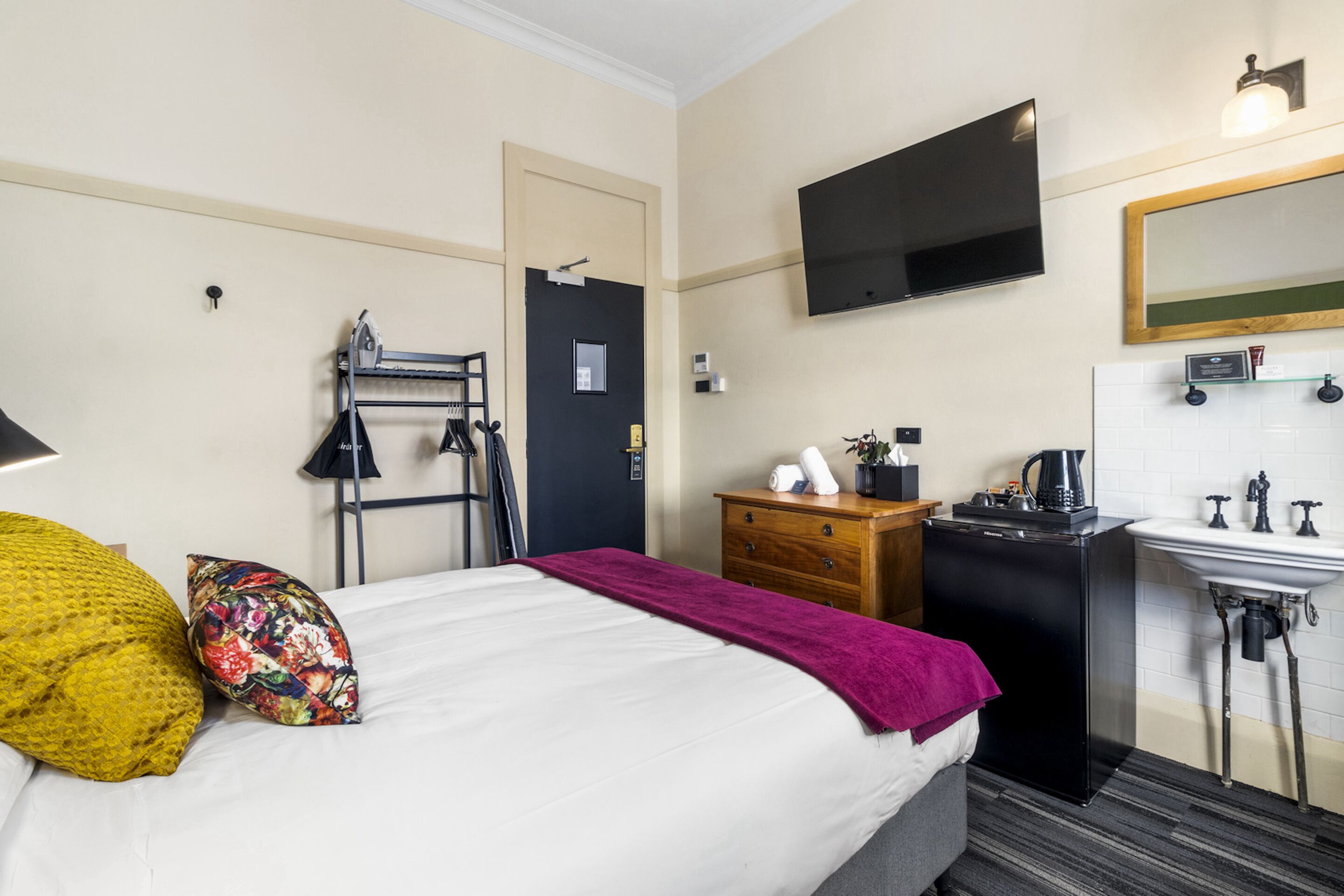 Une chambre d’hôtel équipée d’un lit, d’une commode, d’une télévision, d’un miroir, d’un lavabo et d’une machine à café.