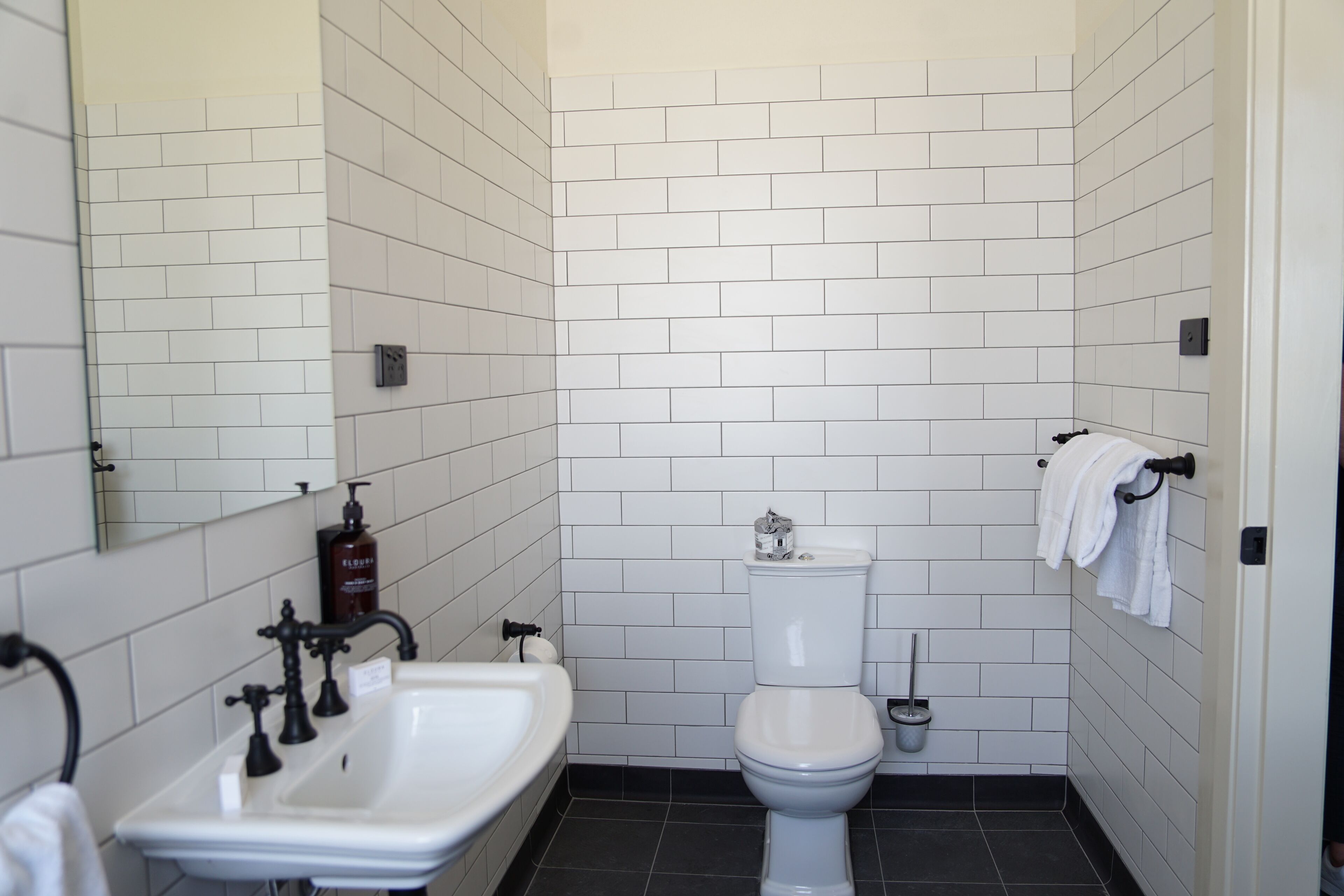 Un baño con paredes de azulejos blancos, un lavabo blanco, un inodoro y un secador de manos.