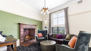 A modern living room with a brick fireplace, a round coffee table, and a sofa with multiple cushions. - Hotel Queanbeyan Canberra (Queanbeyan)
