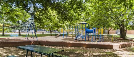 A park with a playground, picnic table, and benches.