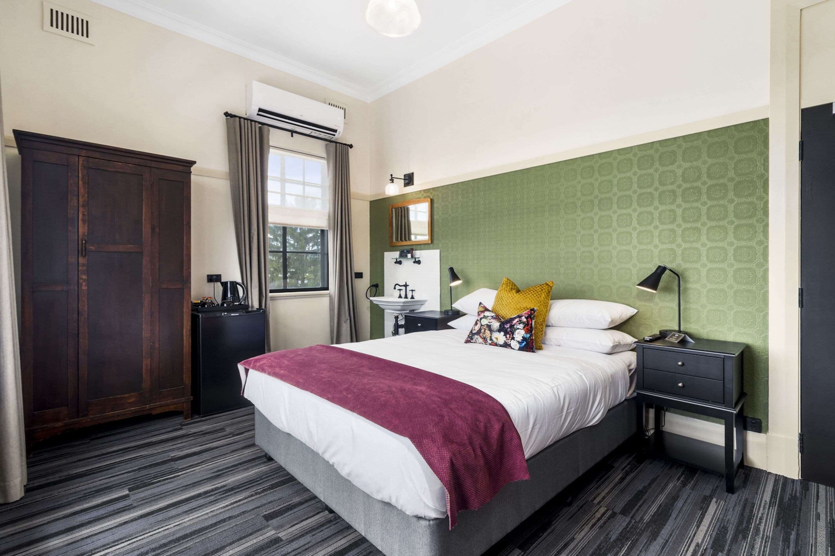 A hotel room with a large bed, a wardrobe, a bedside table with a lamp, and a window with curtains.