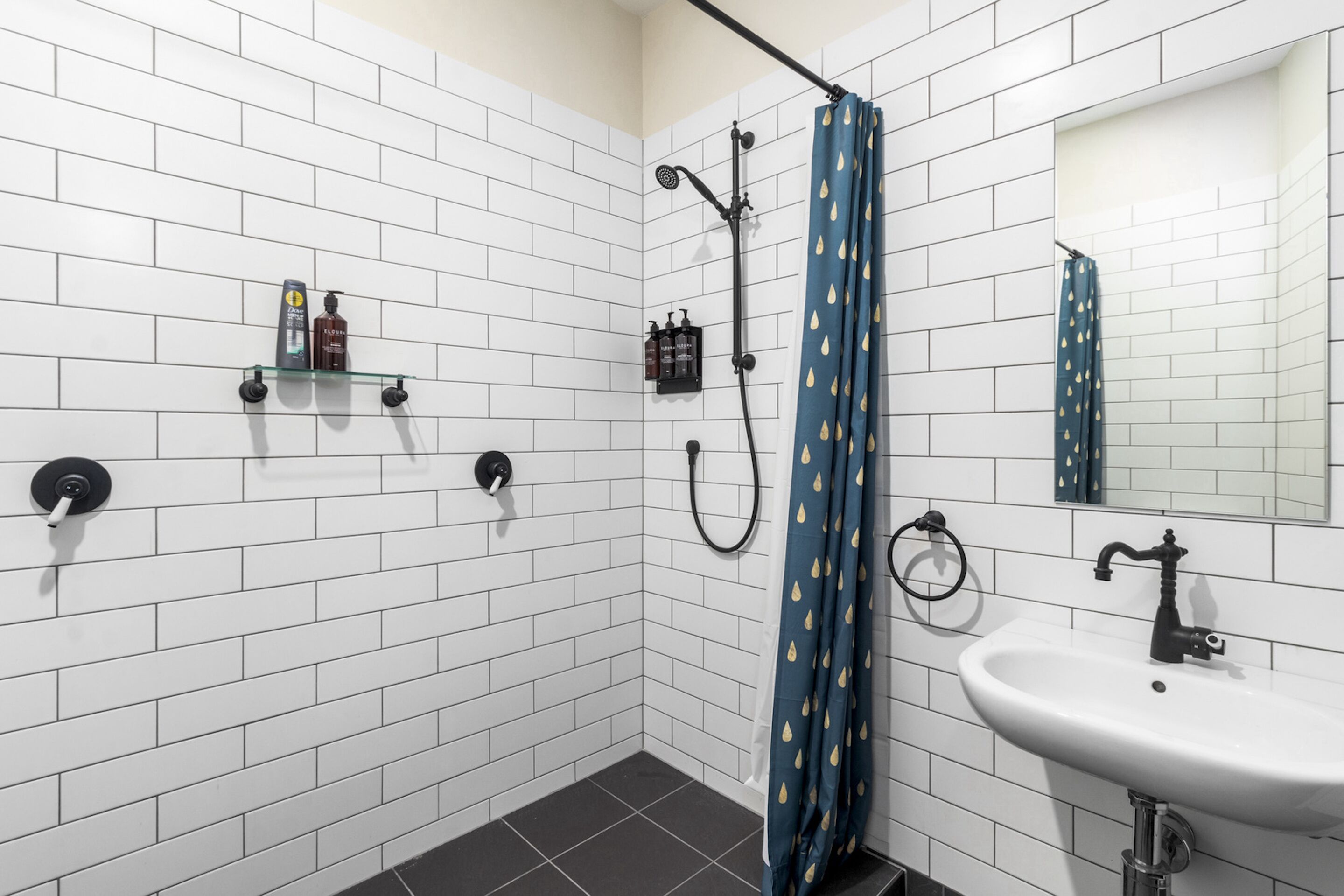 A bathroom with white tiled walls, a shower with a blue shower curtain, a sink, and a mirror.