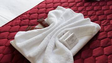 A neatly folded white towel with a Flora brand label on a red quilted bedspread.