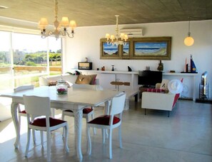 A modern living room with a dining area, white furniture, a television, and artwork on the wall.