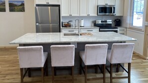 A modern kitchen with white cabinets, stainless steel appliances, and a marble island with bar stools. - The White House- Suite B Upstairs (Silverton)