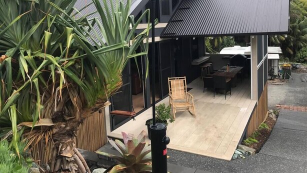 A modern house with a covered patio, outdoor furniture, and large green plants.
