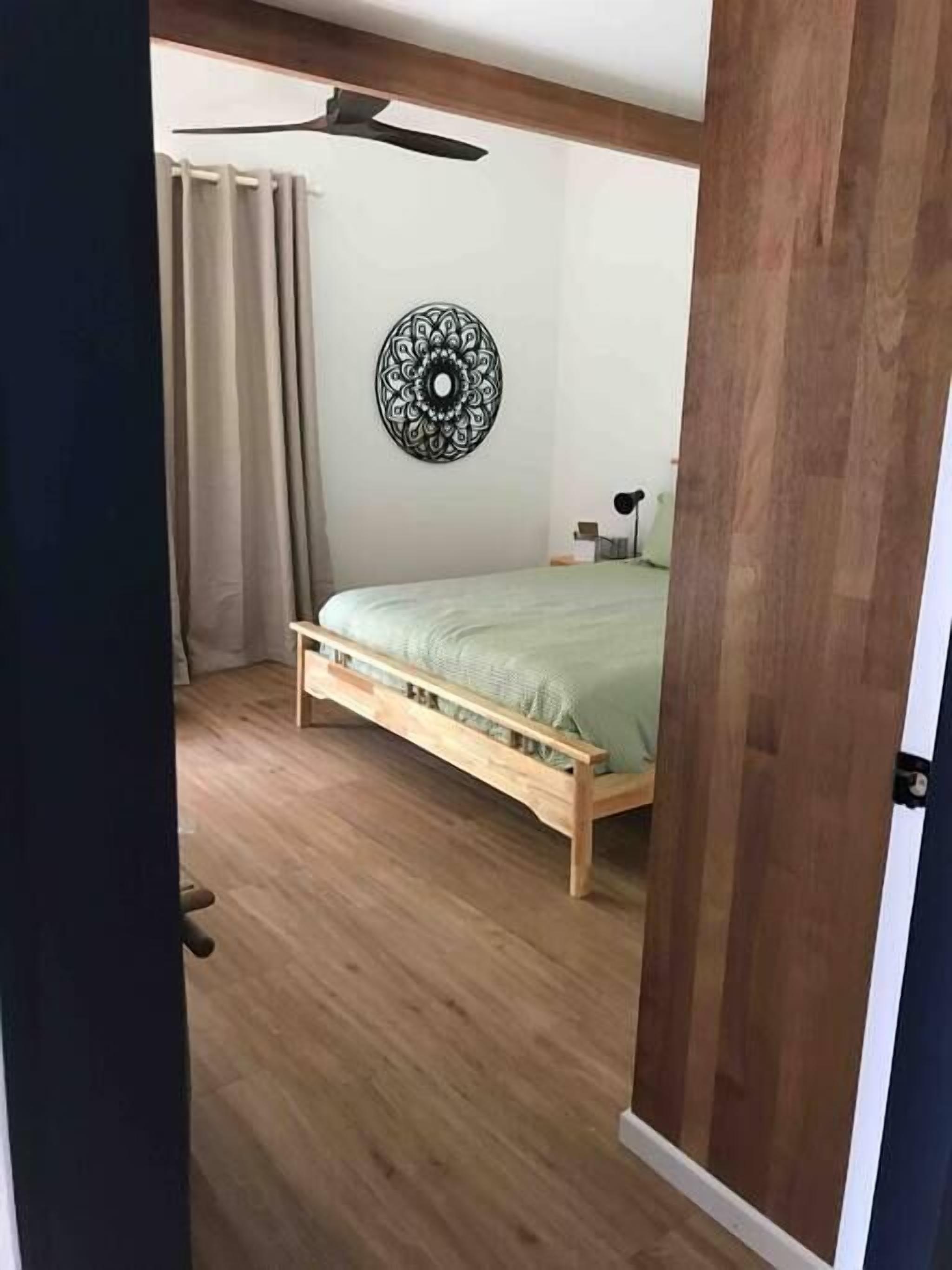 A bedroom with a wooden bed, a ceiling fan, a wall decoration, and a window with curtains.