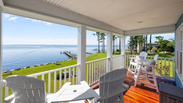 A covered porch with white Adirondack chairs, a wooden table, and a view of the water and dock. - Neuse Village #3 - Check out the amazing views! (Arapahoe)
