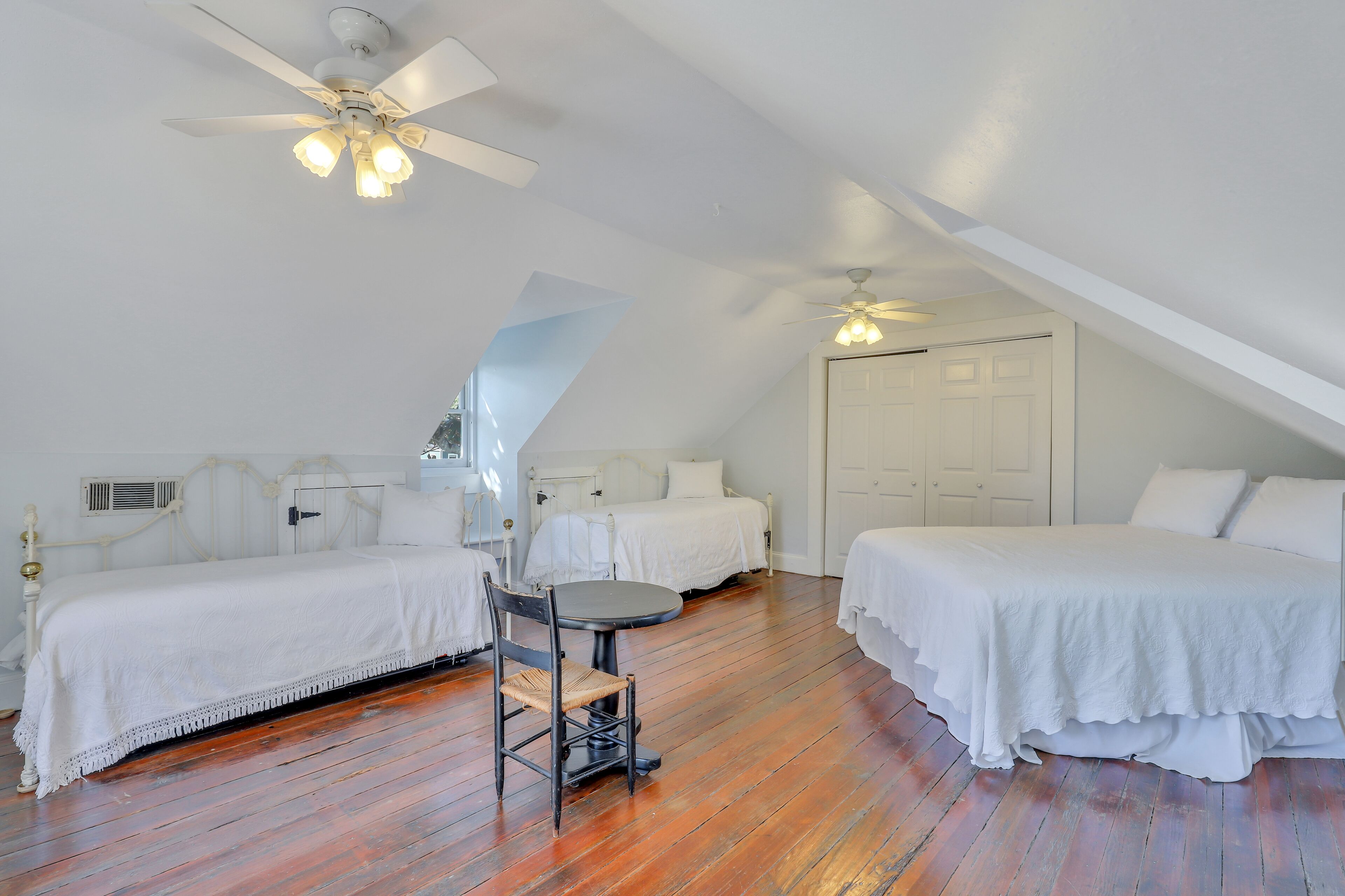 A room with two beds, a dining table, and a ceiling fan.