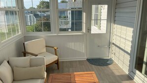 Un solárium con ventanas amplias, un banco de madera, una butaca acolchada y una puerta que da al exterior.