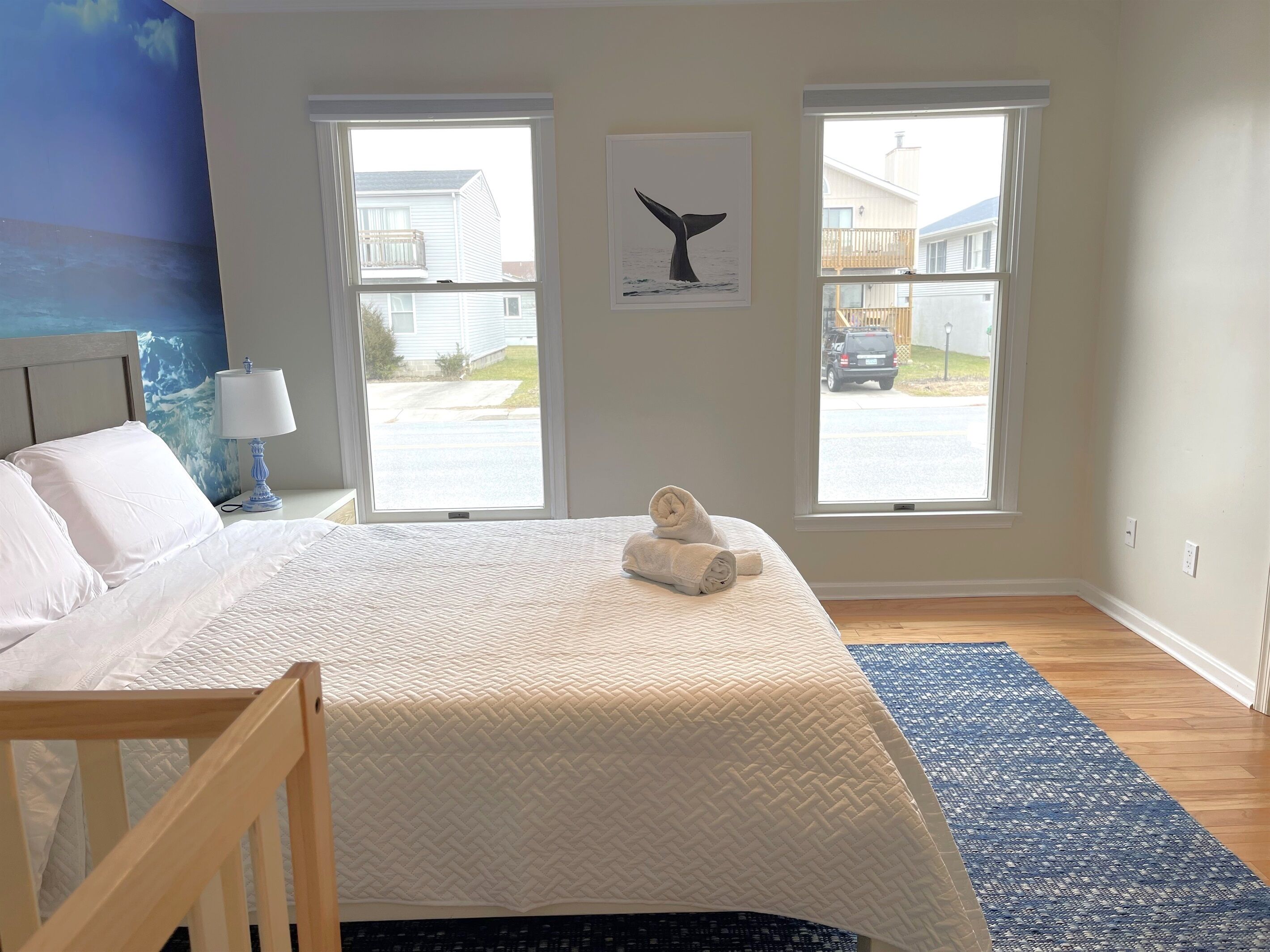 Quarto com cama, duas janelas, quadro de rabeta de baleia na parede e tapete azul.