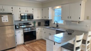Una cocina moderna con armarios blancos, electrodomésticos de acero inoxidable, encimera de granito y un ventanal que proporciona luz natural.