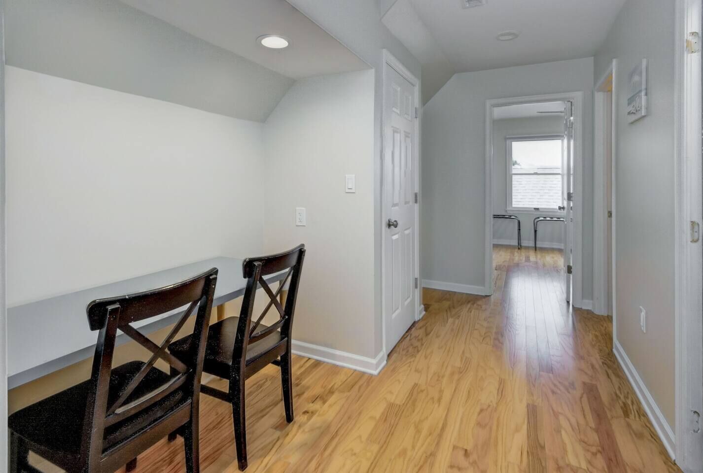 A hallway with wooden flooring, white walls, and two wooden chairs.