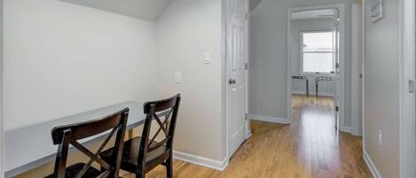 A hallway with wooden flooring, white walls, and two wooden chairs.