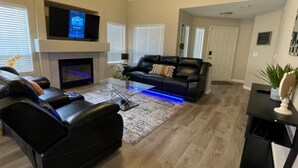 A living room with a fireplace, a black leather sofa, a coffee table, and a flat-screen TV mounted above the fireplace. - Vegas Vacation Home ... Close to The STRIP (North Las Vegas)