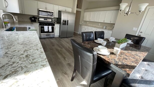 A kitchen with white cabinets, a granite countertop, a dining table with chairs, and a built-in oven. - Vegas Vacation Home ... Close to The STRIP (North Las Vegas)