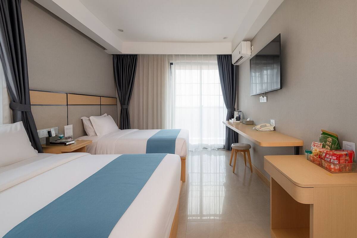 A hotel room with two beds, a desk, a chair, a TV, and a minibar.