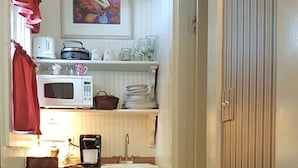 A kitchen with a microwave, coffee maker, and shelves with dishes and glasses.