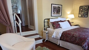 A bedroom with a bed, a chair, a nightstand, and a staircase leading to a closet.