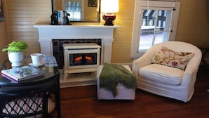 A cozy living room with a fireplace, a comfortable armchair, a small table with a plant, and a bookshelf.