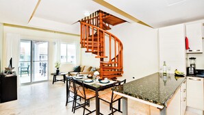 Een moderne keuken met een spiltrap, een eethoek met een tafel gedekt voor vier personen, en uitzicht op het buitenbalkon.