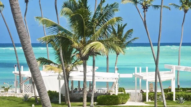 Een resort met een witte kiosk met uitzicht op een strand met palmbomen en turquoise water.