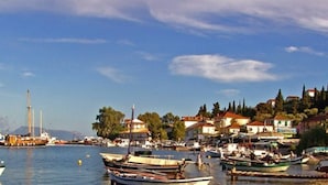 A coastal town with boats docked along the waterfront, buildings with red roofs, and a clear sky.