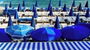 A beachside view with rows of blue-striped umbrellas and lounge chairs facing the ocean.