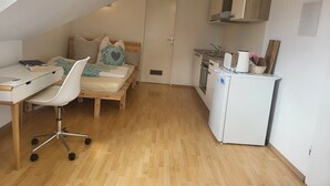 A compact, well-lit room with a bed, a desk with a chair, a kitchenette, and a door. - Stunning 1-Bed Apartment in Bodolz Lake Constance (Bodolz)