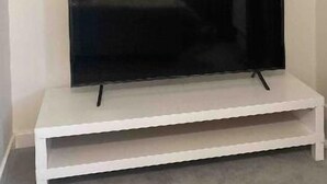 A flat-screen TV on a white stand in a room with plain walls. - 2 Bed House - Sleeps 4 - Parking - Wifi (Leeds)