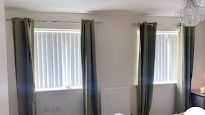 A bedroom with two windows, a radiator, a white bed, and a chandelier. - 2 Bed House - Sleeps 4 - Parking - Wifi (Leeds)
