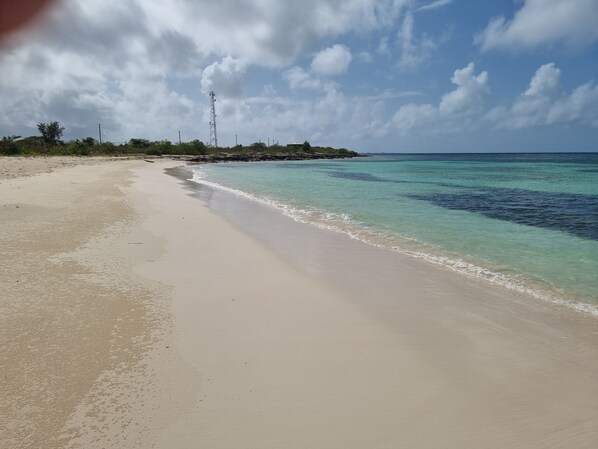 A beach with clear turquoise water, a sandy shore, and a communication tower in the distance. - Charming 1-Bed Cottage in Codrington (Codrington)