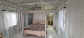 Simple, functional room with a central bed, small dining table, and ceiling fan.