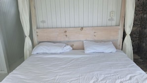 Un letto con testiera in legno, biancheria da letto bianca e una parete in pietra sullo sfondo.
