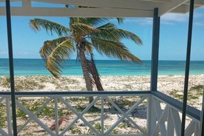 A beach view from a covered area with a palm tree and clear blue water.