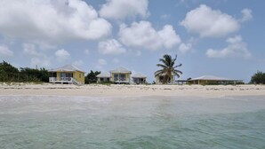 Una proprietà sulla spiaggia con diversi edifici gialli, una palma e acque turchesi cristalline.