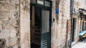 Un bâtiment en pierre avec une porte noire, un escalier à l’intérieur et une table bleue à l’extérieur.