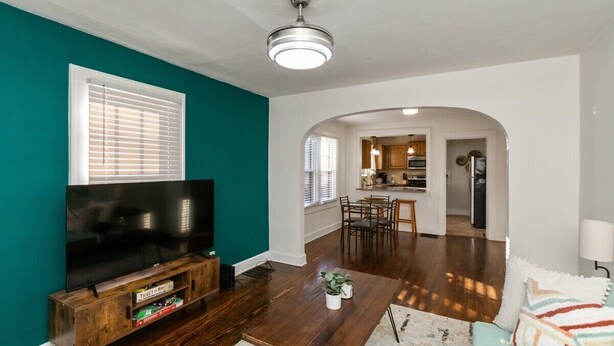 A living room with a TV, wooden entertainment unit, and a coffee table. There is a kitchen visible through an archway. - Downtown 2 BR Retreat / Discounts for Longer stays (Indianapolis)